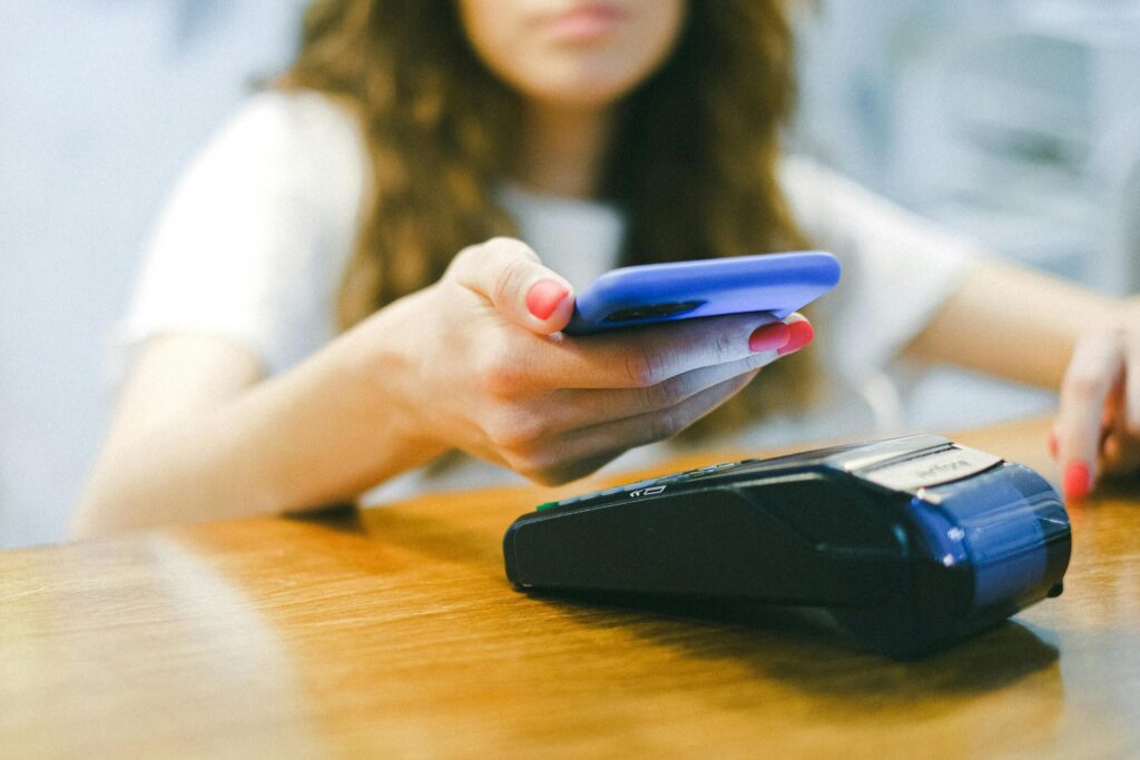 A woman processes a contactless payment using her smartphone at a payment terminal.